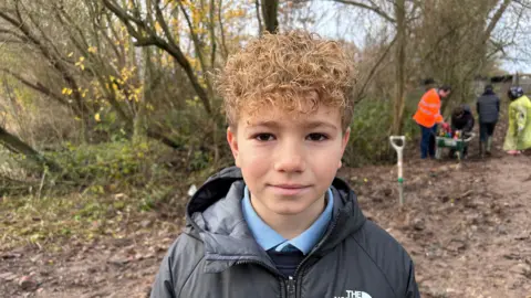 A young boy with blonde curly hair standing on the sides of the water dyke