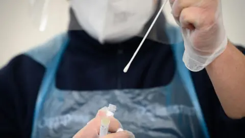 Getty Images A member of the medical team holds up a used swab from a PCR test at Gatwick Airport