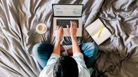 Getty Images A man works on a laptop on his bed