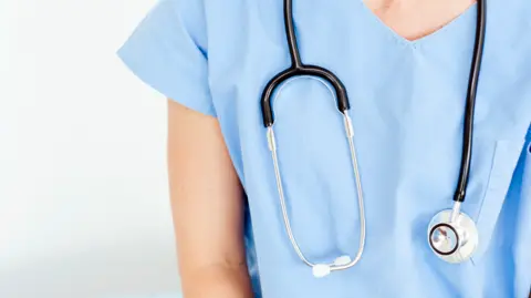A stethoscope is around a medical person dressed in light blue, whose face is not seen, in this generic photo.