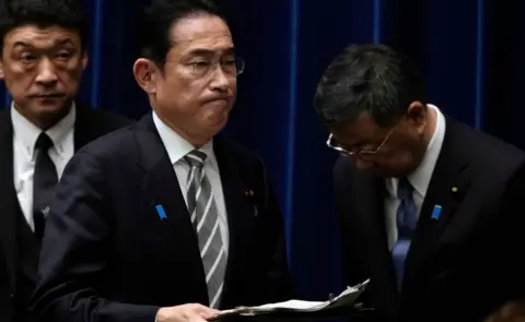 EPA Japanese Prime Minister Fumio Kishida (C) walks past the disgraced Chief Cabinet Secretary Hirokazu Matsuno