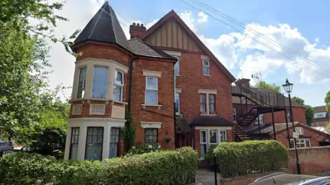 Google Hepworth House is a large multistory detached house with an iron external staircase. There is a shoulder-high bush surrounding the perimiter