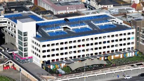 Aerial image of a multi-storey car park. It is a large white building but with dirty marks across the front of the building.