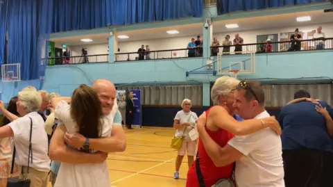 BBC Two men hug women in a sports hall.