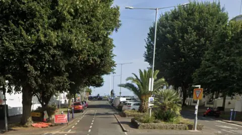 A Google maps screenshot of Devonshire Place in Eastbourne - a dual carriageway lined with trees and a palm tree in the middle. The sea is at the end of the road. 