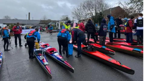 BBC Canoeists wearing wetsuits and lifejackets carry out checks on their canoes and kit