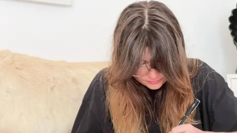 Abi leads over a drawing pad with a pen as she focuses on her work