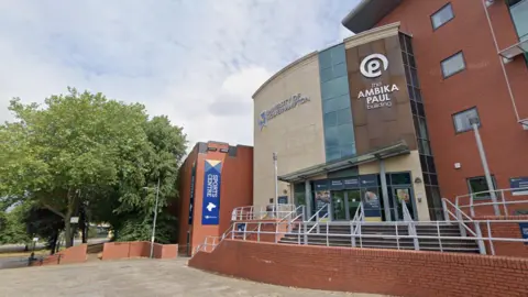 LDRS University of Wolverhampton buildings which are primarily red brick with a stone and glass frontage. To the right of the frontage is a white sign which reads: The Ambika Paul building. 