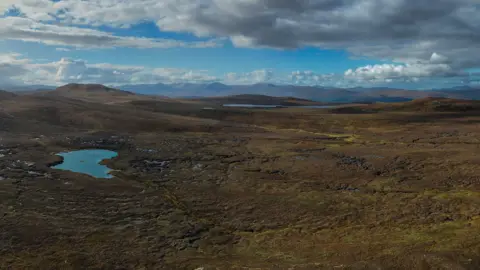 Tracks Ecology Limited A wide open stretch of peat bog and moorland. A large pool can be seen on the left hand side of the picture. There are no trees to be seen. The sky is a dramatic with blue colours and white and grey clouds.