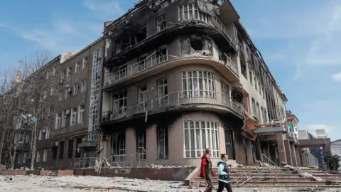 Reuters Residents walk past a destroyed building in the Ukrainian city of Mariupol