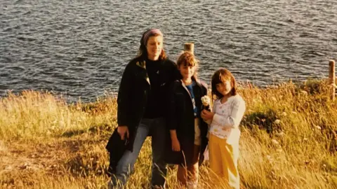 Joan Edgington Joan in the 1980s as a young mum with her two girls in front of water