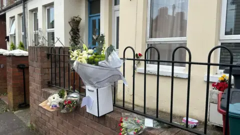 Bouquets of flowers siting on a wall outside a terraced house.