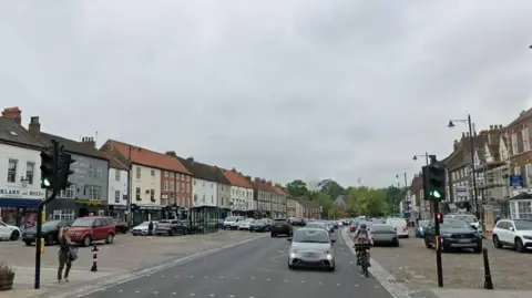 Google Streetview of Yarm town centre. A number of vehicles are travelling along a main road near traffic lights. Other vehicles are parked to either side of the road.