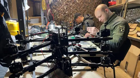 Paul Pradier/BBC Uniformed Ukrainians in a workshop repair drones for use on the battlefield