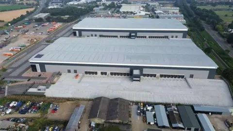 SIZEWELL C Two large, grey warehouses are pictured from above next to the A 14 road 