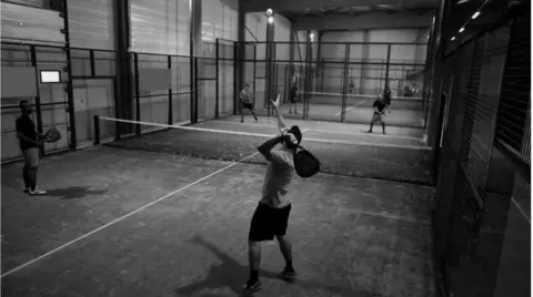 Ellis Healy Architecture/York Council Image of men playing padel inside a building with a low net across the court