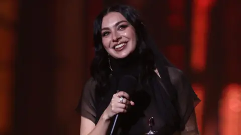 Getty Images Charlie XCX en el podio, nuevamente, para recibir otro británico. Lleva un vestido negro transparente y tiene su cabello oscuro.