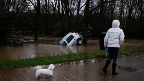 Reuters A woman walks past a submerged car during floods following heavy rainfall in Villava, Spain, December 10, 2021