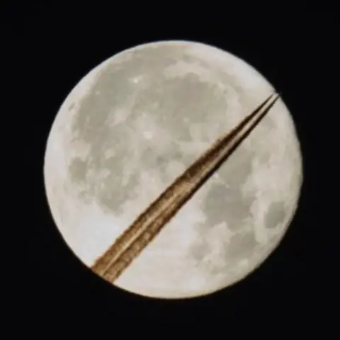 Frank Gardner The supermoon appears with trails from an aircraft juxtaposed against it