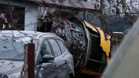 AFP via Getty Images Wreckage of the plane, which looks to be an engine, in a residential area, with a car parked in front of a house