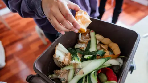 A boy throws an apple core into a food recycling caddy that is filled with peelings