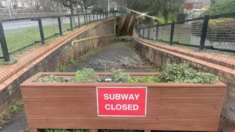 Toby Friedner/BBC A red sign saying "Subway closed" is fixed to a large planter blocking the entrance to the St Mary's Way underpass.