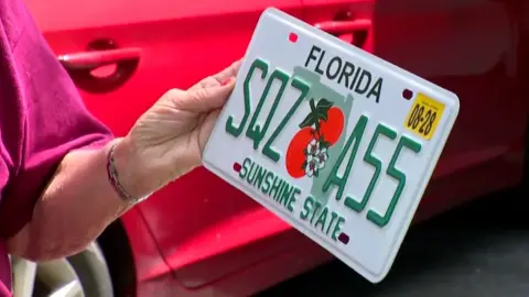 The woman holding the license plate that says SQZ A55