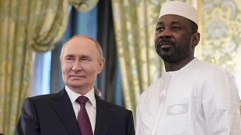 Russian President Vladimir Putin (left) in black suit and white shirt and Mali's junta leader Assimi Goita in a white robe and white cap