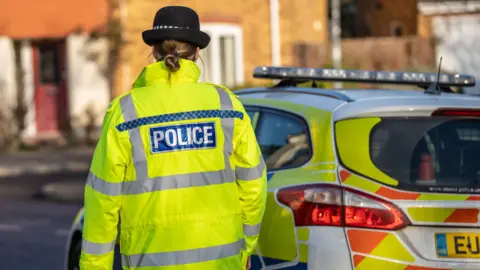 PA Media An Essex Police officer stood next to a police car