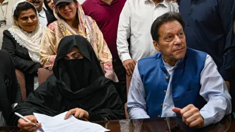 Getty Images De voormalige Pakistaanse premier Imran Khan (R) kijkt samen met zijn vrouw Bushra Bibi (L) toe terwijl hij op 17 juli 2023 borgstellingen tekent in verschillende zaken bij de burgerlijke stand van het Hooggerechtshof in Lahore.