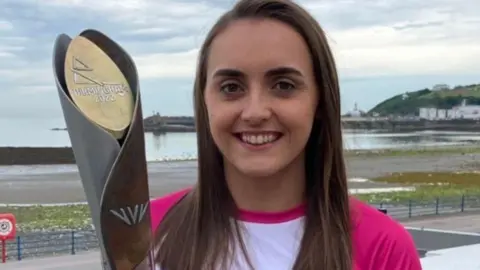 ERICA BELLHOUSE Kinley wearing a pink and white top holding the 2022 Commonwealth Games baton.