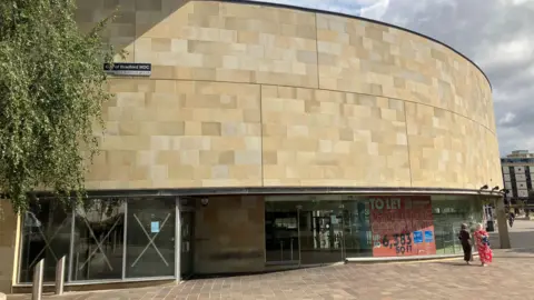 A retail building with glass windows along the first floor and a stone facade on the second floor.