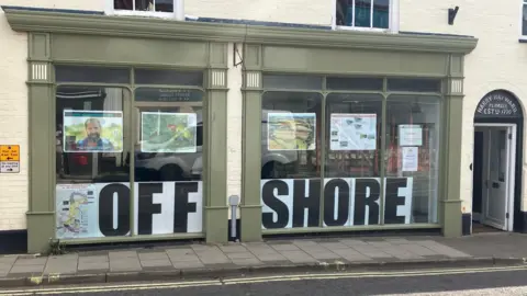 GUY CAMPBELL/BBC A green shop facade with the slogan "Offshore" written in large capital letters in the front window.