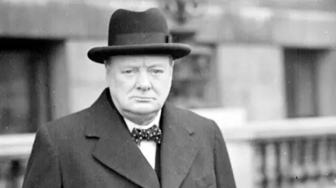 PA Sir Winston Churchill wearing a black hat and overcoat and a spotted bow tie