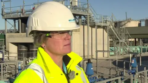 Nicola Shaw in a helmet and high vis jacket stood in front of a sewage works