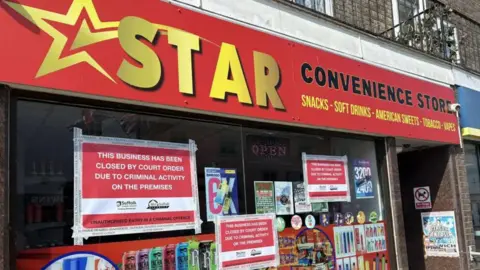 The frontage of Star Convenience store in Stowmarket. Advertisements are on the windows and bright red signs which confirm the business "has been closed by court order". 