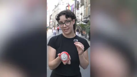 A person with short, dark curly hair wearing a black t-shirt took to the camera