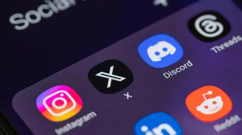 A stock image showing a close up of a smartphone screen with the logos of Instagram, X, Discord, Threads, LinkedIn and Reddit visible on a dark background