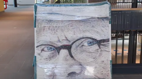 Bradford Council One square of the David Hockney portrait featuring a close-up of the painter's bespectacled face, standing against some railings