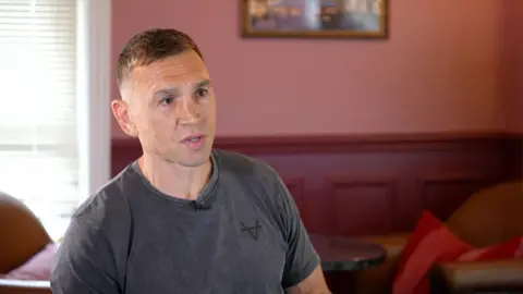 Kevin Sinfield wears a black shirt during an interview