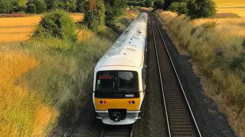 Chiltern Railways An overhead view of the full length of a train on a line surrounded on either side by tall grass, bushes and fields. There is another railway line which has no trains on it.