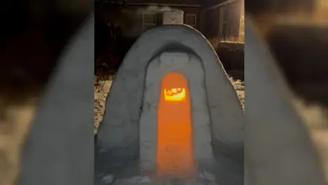 A fire glows bright orange inside an igloo in a garden in Orkney