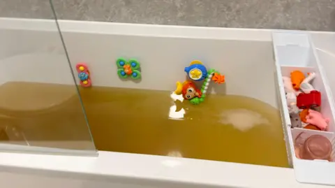 Handout The bath, which has kids toys on it, is filled with brown water.