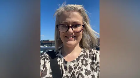 Supplied Joanne Howey is smiling at the camera. She has straight blonde hair and black-rimmed glasses. She is wearing a beige top with a brown pattern.