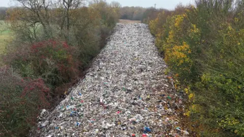 Billy Burnell A pile of waste extends like a river between lines of trees into the far distance.