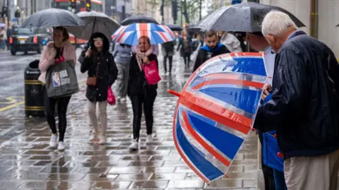 Older man holding union jack umbrella on Oxford Street looking at other shoppers