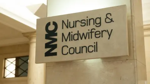 Nursing and Midwifery Council Nursing and Midwifery Council sign in black writing on a stone plinth and stone wall.