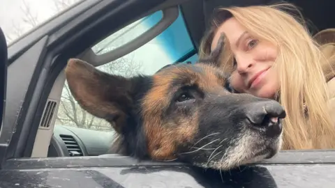 Lala Tarapakina/12 Guardians A woman with blonde hair with a dog in a car