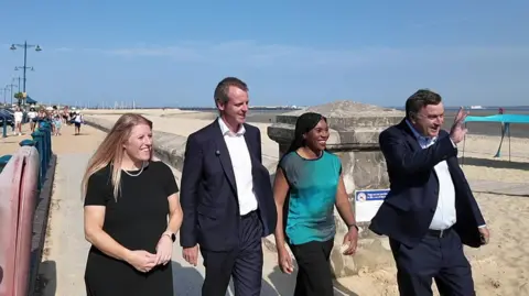 Kemi Badenoch walking along the Isle of Wight seafront on a sunny day with Donna Jones, Joe Robertson MP and shadow chancellor Mel Stride