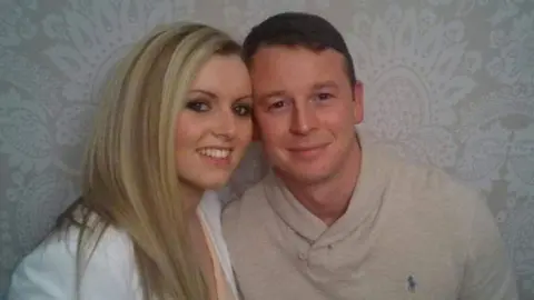 Samantha Jones Samantha and Trevor smiling into the camera when they were younger. The side of their heads are touching and they're standing in front of a grey, patterned wall.